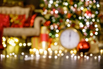 Naklejka premium Blurred bokeh lights shining warm white light near the Christmas tree and gifts on cozy winter evening. Concept of New Year and Christmas meeting and pleasant holiday atmosphere. Advertising space
