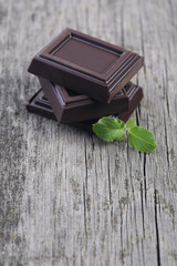 Dark chocolate with leaves on wooden background