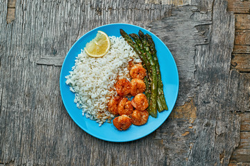 Delicious teriyaki coated shrimps stir fry with grilled asparagus, rice and sesame on a blue plate. Healthy seafood meal. Top view, directly above shot.