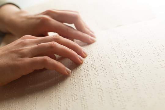The hand of a blind man reads the text of a braille book.