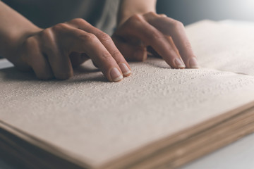 The hand of a blind man reads the text of a braille book. - obrazy, fototapety, plakaty