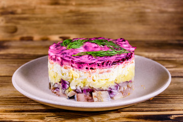 Ceramic plate with russian traditional new year salad herring under fur coat (shuba) and on rustic wooden table