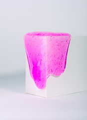 Slime, bright pink toy flows down of white box, against white background.