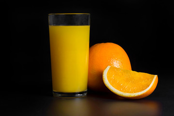 A glass of fresh orange juice and slices of orange on a black background, close-up. © Andrii