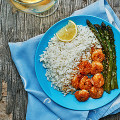 Shrimps and asparagus stir fry with rice on a blue plate with sesame seeds. Delicious seafood meal. Top view, directly above shot.
