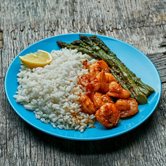 Delicious teriyaki coated shrimps stir fry with grilled asparagus, rice and sesame on a blue plate. Close-up shot.