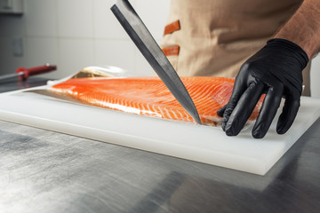 The cook unpacks the salmon fillet with a knife on a cutting Board.