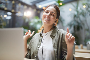 Portrait of carefree young woman listening to music while working on cafe terrace and dancing, copy space