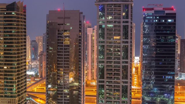 Residential and office buildings in Jumeirah lake towers district night to day transition timelapse before sunrise in Dubai. Aerial panoramic view from above with illuminated modern skyscrapers
