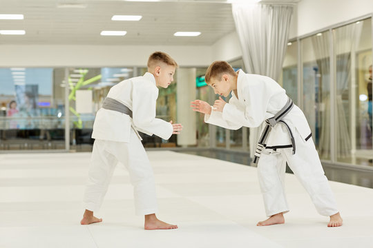 Two young judoists in kimono standing and fighting with each other in the gym