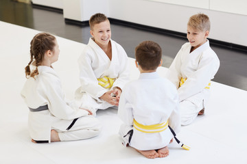 Group of children sitting on the floor together and talking to each other before sport training in karate in the gym