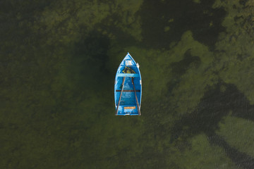 Blue rowing boat floating alone on blue green ocean water aerial