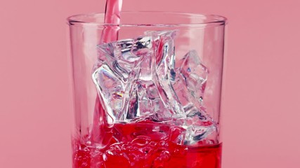 Pouring red soft drink into a glass with ice cubes on pink background, slow motion shot on Red - Powered by Adobe