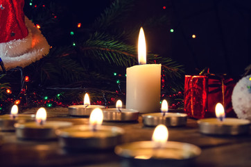 Many candles on a wooden background, branches of a Christmas tree, a red cap. Beautiful, magical Christmas and new year background