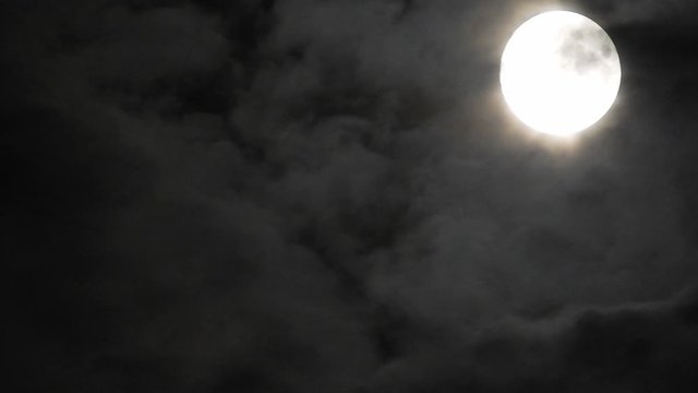 Full moon at night with cloud real time. 4k video full moon in the black sky.  Clouds passing by moon at night. night sky with cloudy weather
