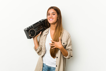 Young caucasian woman holding a guetto blaster laughs out loudly keeping hand on chest.