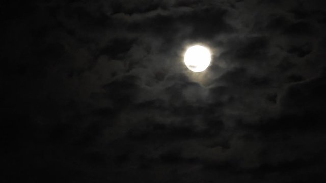 Full moon at night with cloud real time. 4k video full moon in the black sky.  Clouds passing by moon at night. night sky with cloudy weather