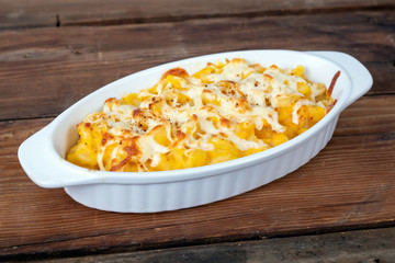 Butternut squash mac and cheese dish closeup on a rustic table and grated cheese on top