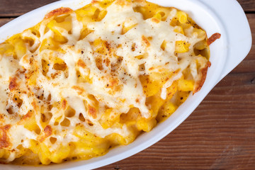 Butternut squash mac and cheese dish closeup on a rustic table and grated cheese on top