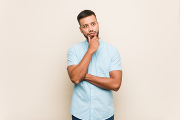 Young south-asian man looking sideways with doubtful and skeptical expression.