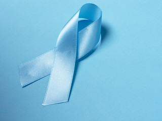 Closeup a Blue satin Ribbon symbol of prostate cancer awareness on a bright blue background. Concept of medicine and health care