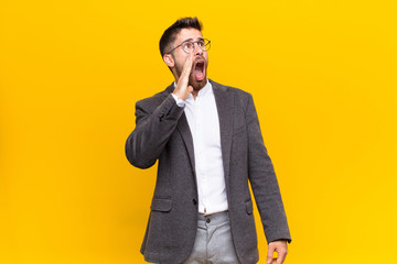 young handosme man yelling loudly and angrily to copy space on the side, with hand next to mouth...