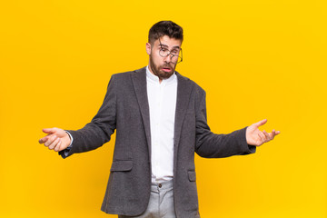 young handosme man shrugging with a dumb, crazy, confused, puzzled expression, feeling annoyed and...