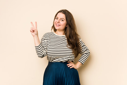 Young curvy woman joyful and carefree showing a peace symbol with fingers.