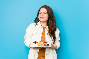 Young curvy woman holding a sweet cakes happy, smiling and cheerful.