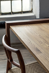 Stylish interior design of dining room in loft apartment with wooden sharing table, chairs,flowers in vase and elegant accessories. Modern home decor. Bright and sunny industrial space. Template.