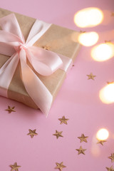 Gift in craft paper with a pink bow on a pink background with holographic sparkles in the form of stars. Template  banner for greeting card your text design 2020. New year, christmas, birthday