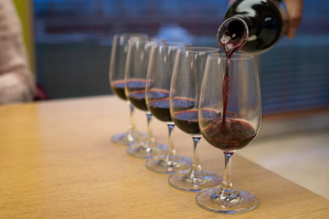 a bottle of red wine is being poured in five glasses placed on a table