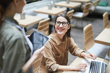 High angle portrait of young woman looking at waitress and smiling while working in cafe , copy...