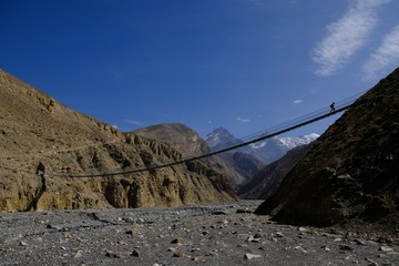 Dramatic view of the hanging bridge over the river and walking tourist in the Kali Gandaki Valley. Nepal, Mustang, Himalaya, trekking around Annapurna
