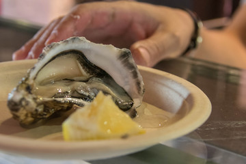 hand taking a fresh raw open oyster with lemon on a plate