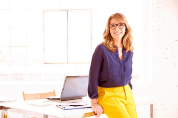 Elegant mature businesswoman standing in the office while looking at camera and smiling