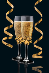 Two elegant perfect glasses filled with sparkling champagne with two gold streamers of serpentine isolated on a black background. Christmas, New Year, anniversary, celebration concept