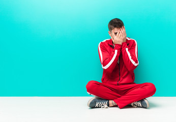 young handosme man feeling scared or embarrassed, peeking or spying with eyes half-covered with...