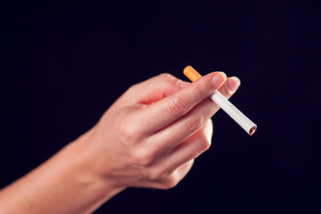 Cigarette in hand on black background. Nicotine addiction concept