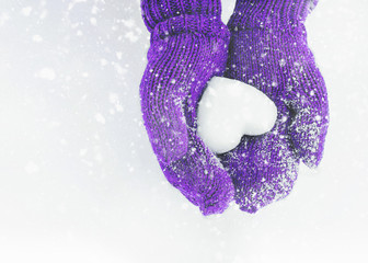 Female hands in knitted mittens with heart of snow in winter day. Love concept. Valentine day background.