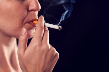Obraz premium Woman smokes cigarette on black background. Nicotine addiction concept