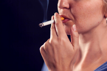 Woman smokes cigarette on black background. Nicotine addiction concept