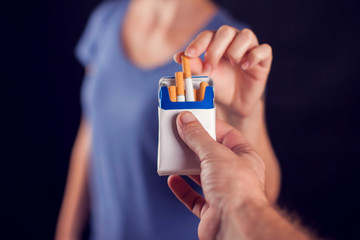 Woman takes cigarette on black background. Nicotine addiction concept