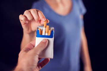 Woman takes cigarette on black background. Nicotine addiction concept