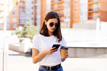 Young woman reading using phone. Female woman reading news or texting sms on smartphone while drinking coffee on break from work.