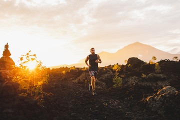 Young male athlete trail running in mountains at sunrise. Amazing black lava volcanic landscape of...