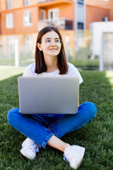 Beautiful young girl with laptop outdoors sitting on the grass