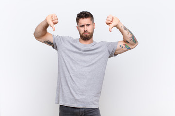 young handosme man looking sad, disappointed or angry, showing thumbs down in disagreement, feeling...