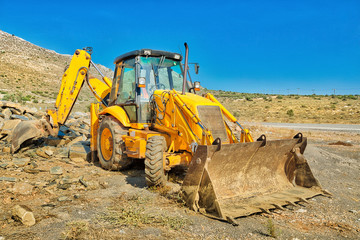 Side view of bulldozer on wheels for mines and pits with a long arms for excavator in mining site. Work in progress, industrial machine. Mining landscape on background.