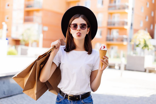 Sale, consumerism, summer and people concept. Happy young woman with shopping bags and ice cream on city street